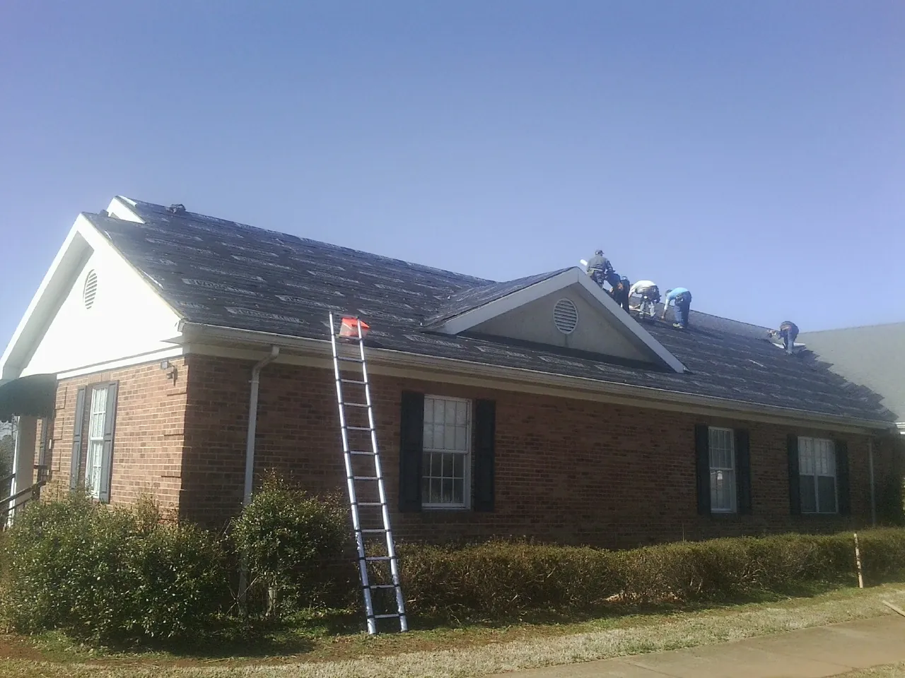 Crew tearing shingles off a brick ranch roof with a ladder set — Emergency Roof Repair work by our crew in Dillsboro