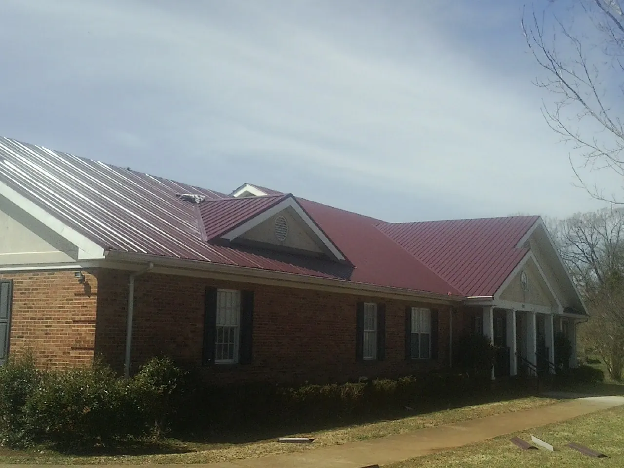 Red metal roof with gabled entries on a long brick building, from a Hail Damage Roof Repair job in Dillsboro