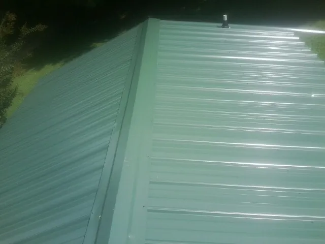 New green metal panels meeting at the ridge of a roof — Flat Roof Repair work by our crew in Dillsboro